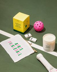 'weekends playing pickleball' candle with pouch and pickleballs on court.