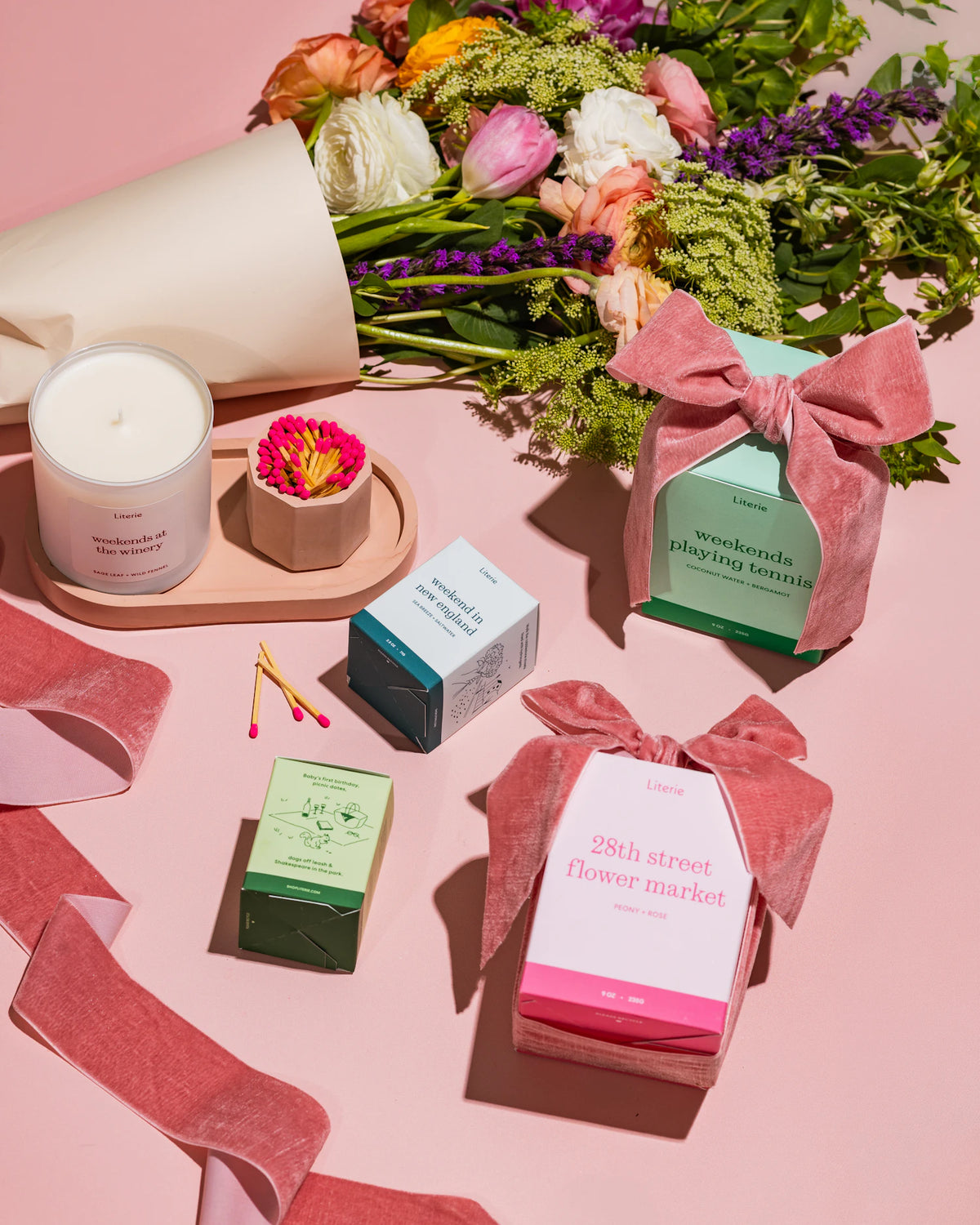 Pink match holder on tray and  items including a candle, flowers, and wrapped gifts on a pink surface.
