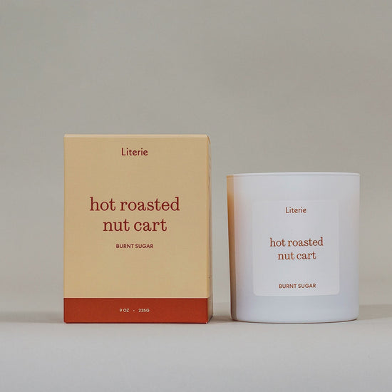 "hot roasted nut cart" candle by Literie sitting next to it's packaging spinning to show and drawn illustration on a light gray background. 