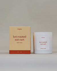 "hot roasted nut cart" candle by Literie sitting next to it's packaging spinning to show and drawn illustration on a light gray background. 