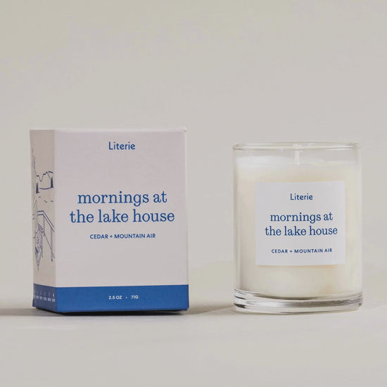 "Mornings at the lake house" little candle box turning and the candle next to it on a light grey background.