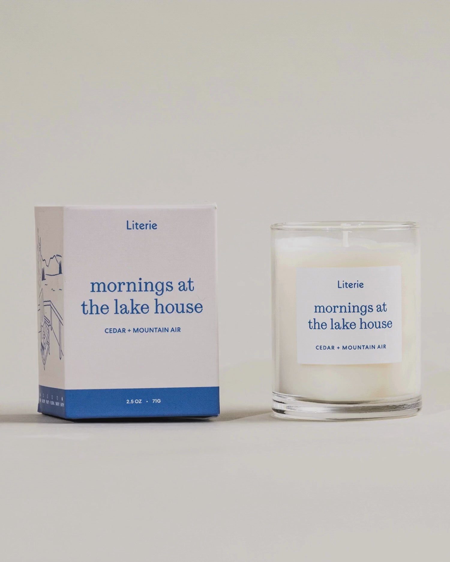 "Mornings at the lake house" little candle box turning and the candle next to it on a light grey background.