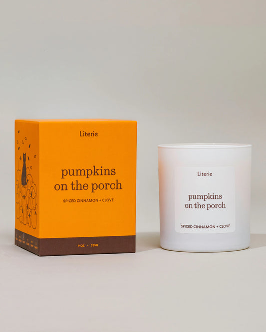 A Literie 'pumpkins on the porch' scented candle shown next to its bright orange packaging box on a neutral light gray background.