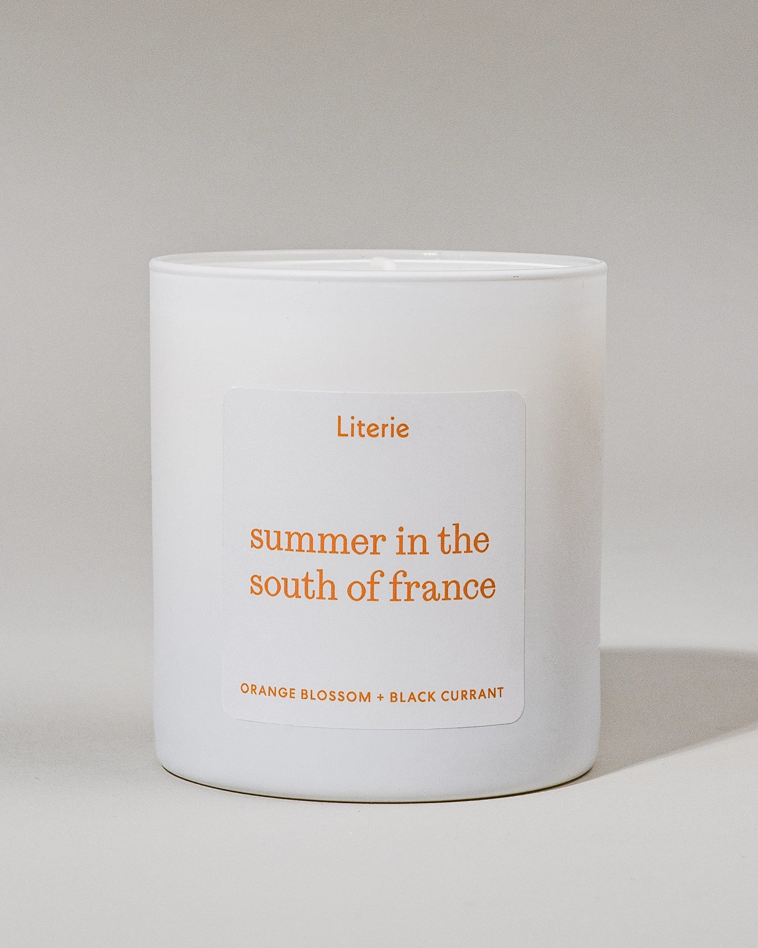 White candle with orange 'Summer in the South of France' and 'orange blossom + black currant' on a light gray background