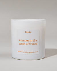 White candle with orange 'Summer in the South of France' and 'orange blossom + black currant' on a light gray background