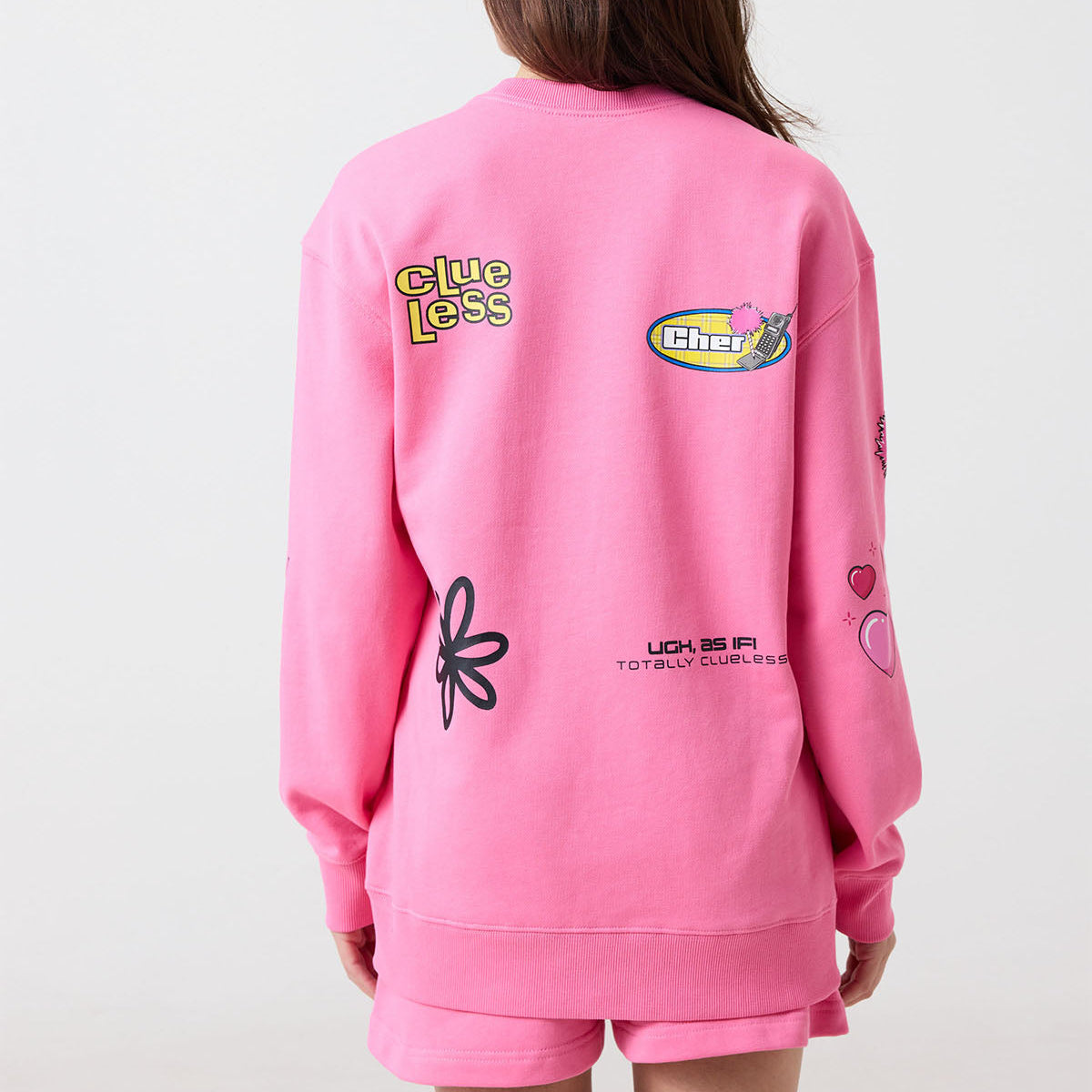 Person wearing a pink Clueless sweatshirt with various logos on the back against a white background