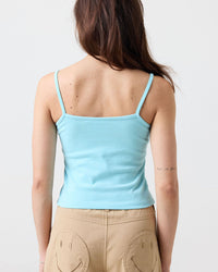 Woman wearing a light blue tank top and beige pants with smiley face designs on a plain background