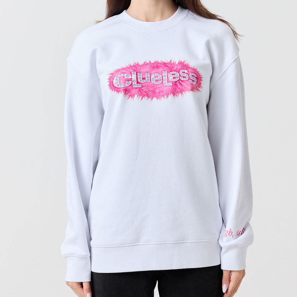 Person wearing a light gray sweatshirt with a pink and white Clueless logo on a plain background