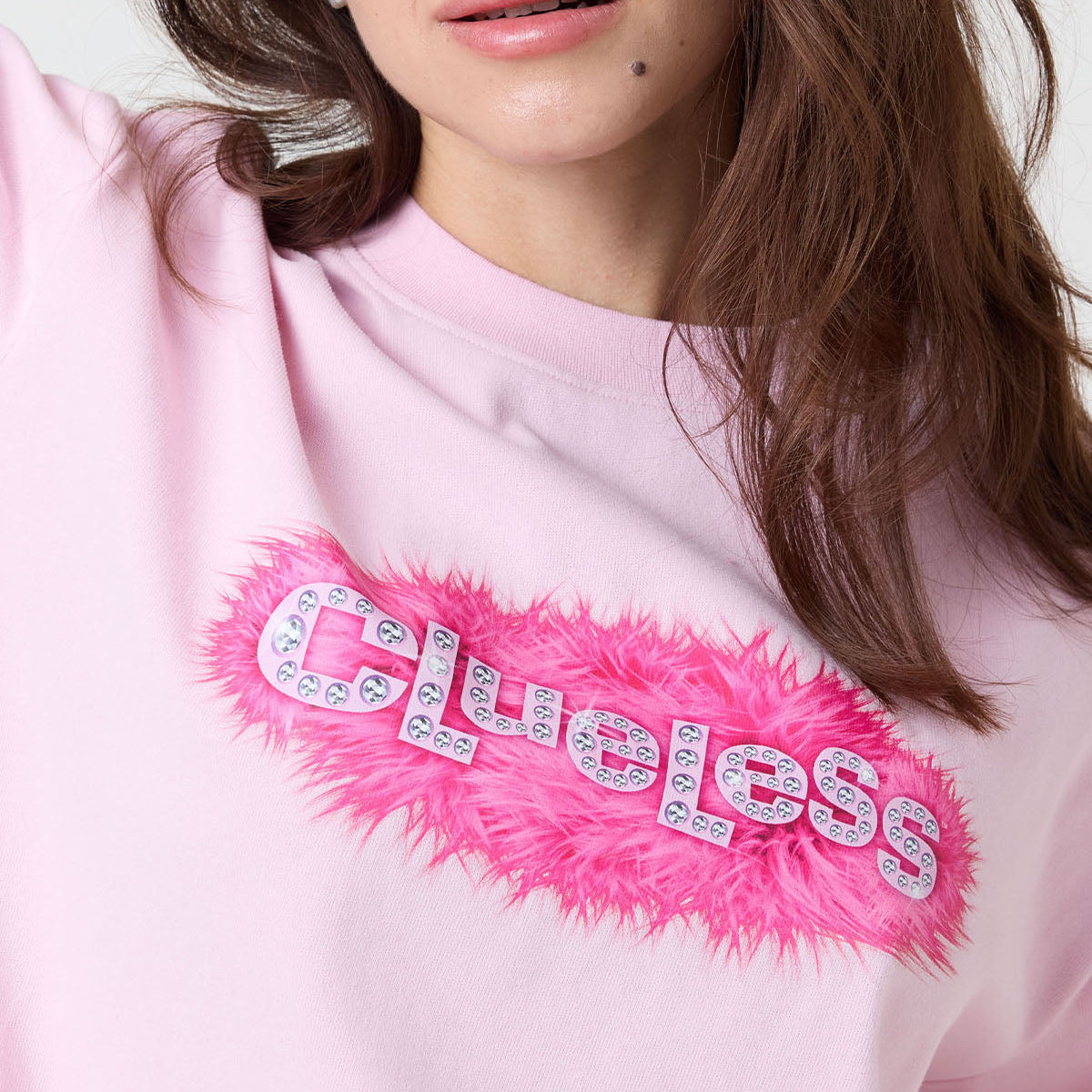 Pink sweatshirt with 'clueless' text and feather detail on a white background