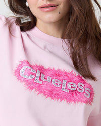 Pink sweatshirt with 'clueless' text and feather detail on a white background