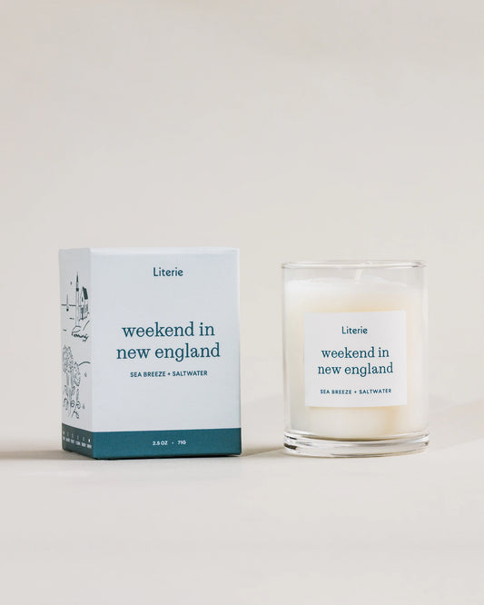 Little candle and packaging labeled 'weekend in new england' by Literie on a neutral background