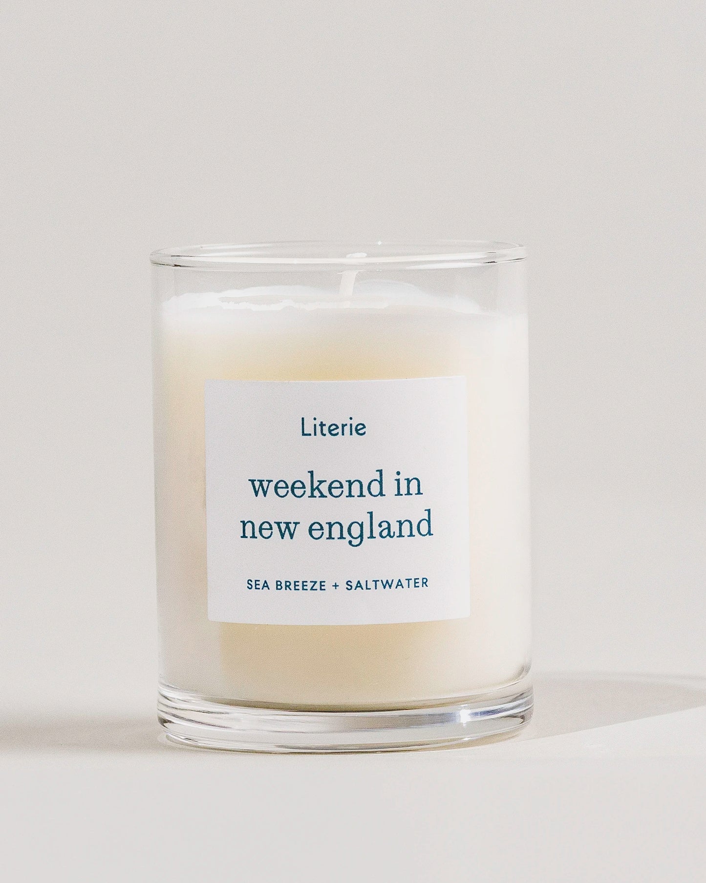 Candle with a label reading 'weekend in new england' by Literie on a light background