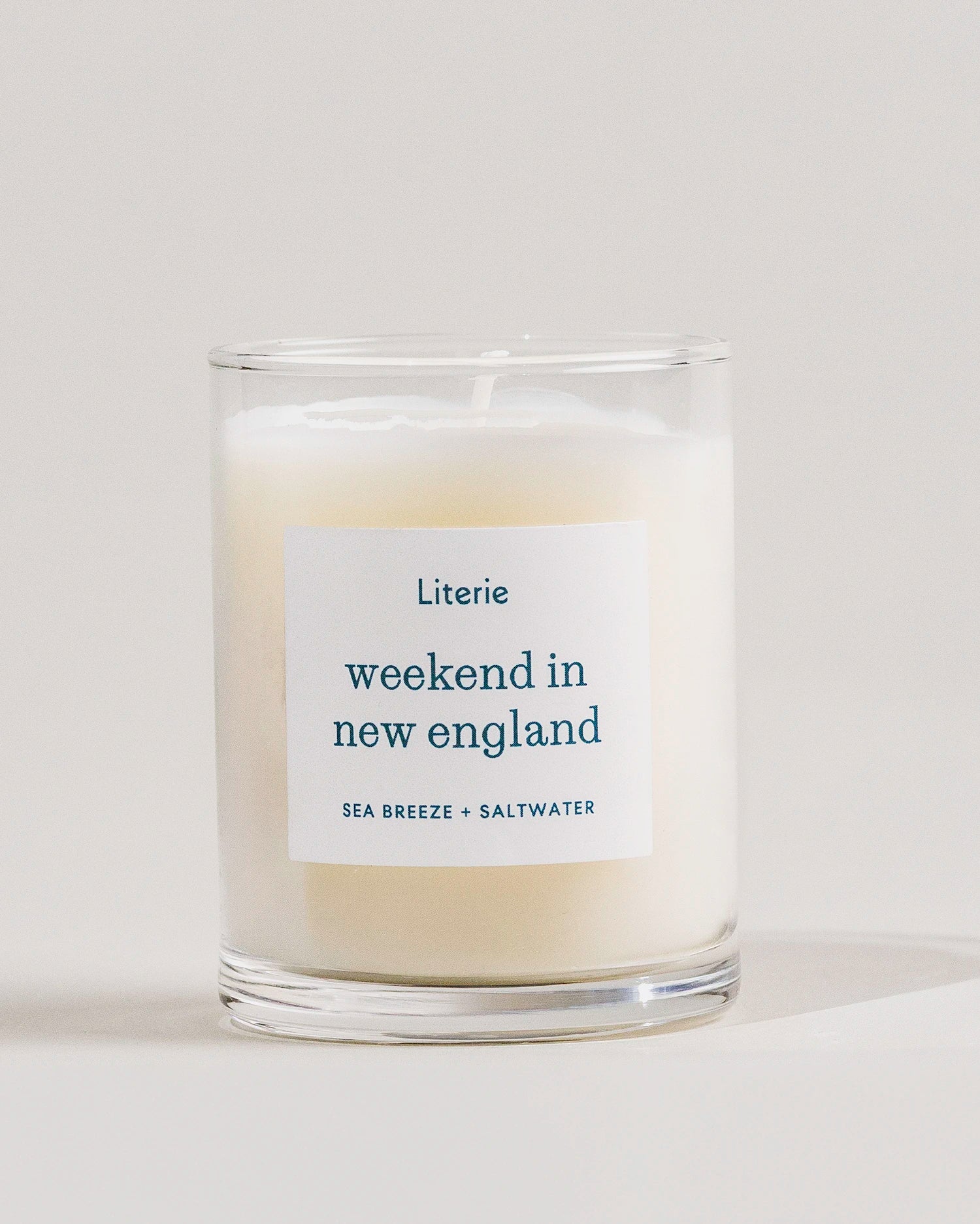 Candle with a label reading 'weekend in new england' by Literie on a light background