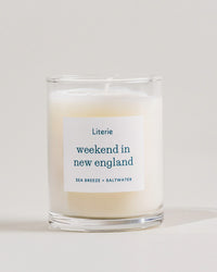 Candle with a label reading 'weekend in new england' by Literie on a light background