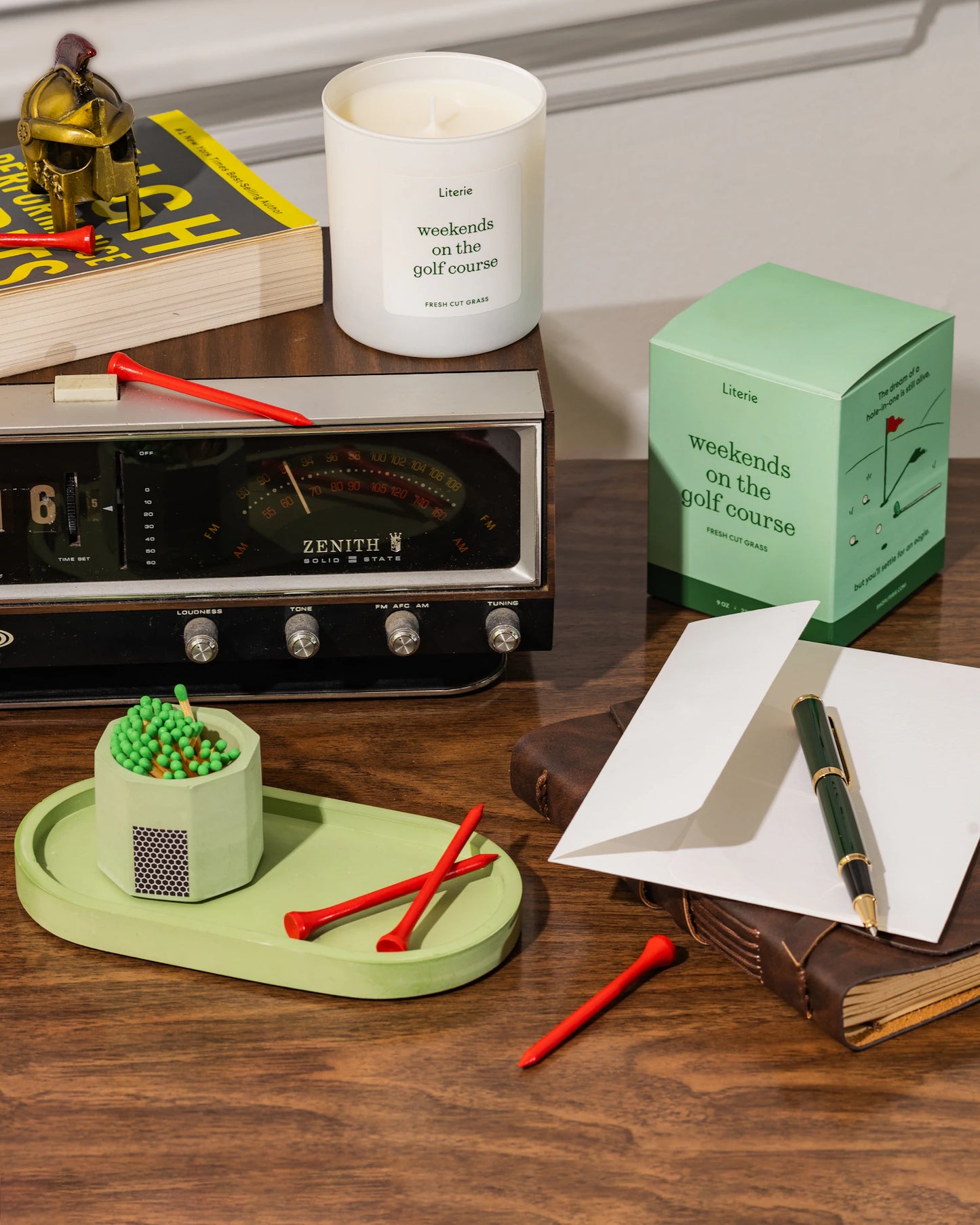 Golf-themed items including a candle by Literie, green candle tray and match holder on a desk.