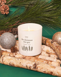 The Christmas Tree Guy candle next to ornaments.